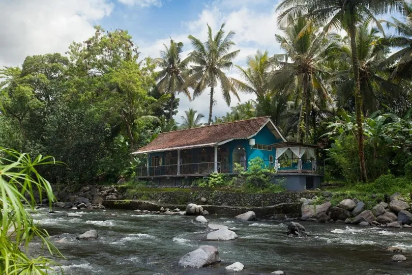 Huisje aan een rivier met palmbomen.