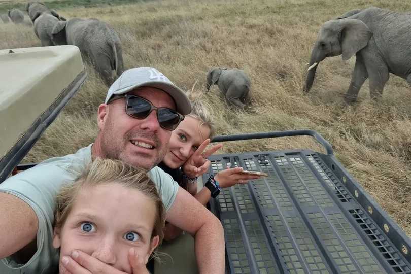 Gezin zit in een safariwagen in Tanzania met olifanten op de achtergrond.