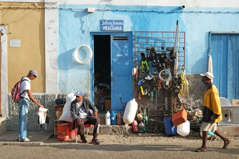 Drie mannen zitten voor een blauw huis op Kaapverdië.