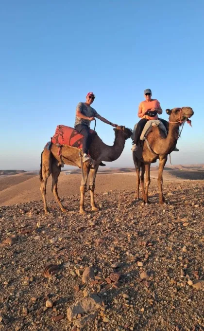 2 reizigers die op een dromedaris zitten in de woestijn.