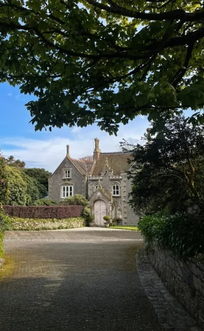 Een charmant, historisch gebouw in Guernsey, omgeven door groen en bomen, met een sierlijke ingang en een rustige oprijlaan.