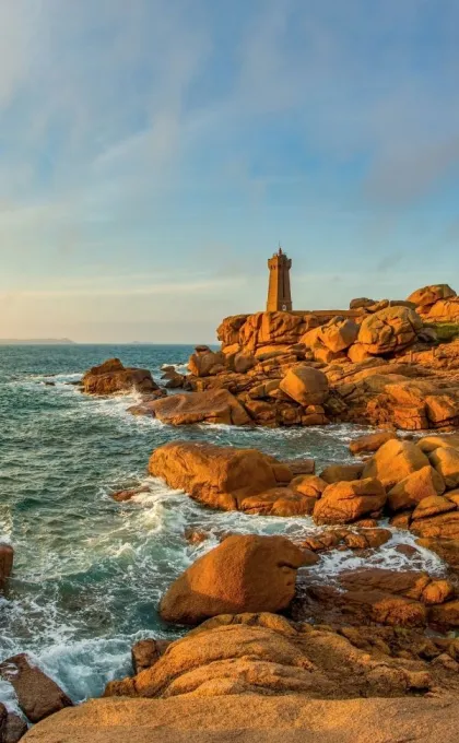 Een roze gloed schijnt op de Roze Granietkust van Bretagne, op de klif staat een stenen vuurtoren.