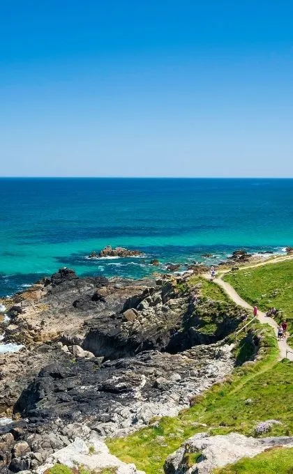 Kust met rotsen en groene weide aan een blauw groene zee.
