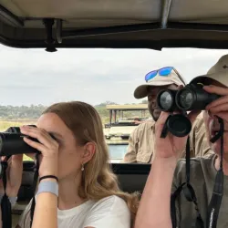 Een gezin kijkt door verrekijkers naar de dieren vanuit een jeep op safari in Tanzania.