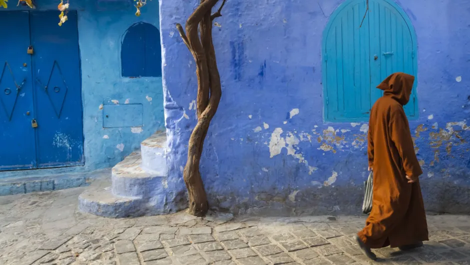 Een persoon in een bruine gewaad loopt langs een felblauwe muur.