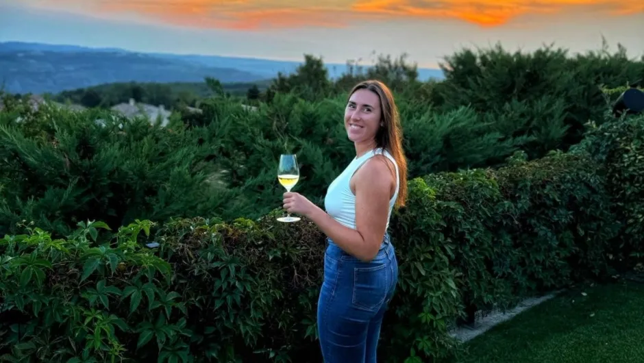 Reisexpert Melissa die een glas witte wijn vast houdt met prachtig groen uitzicht.