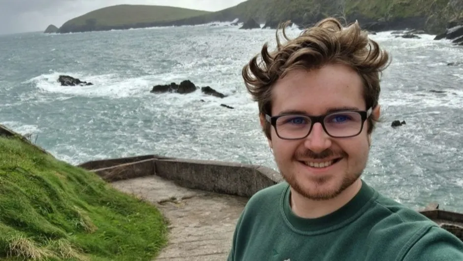 Reisexpert Clément staat op een pad langs de kust met een ruige zee.