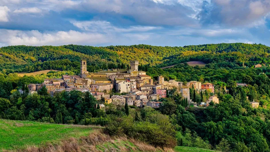 Middeleeuws dorp op een heuvel in Toscane, met stenen huizen en torens, omringd door groene heuvels en bossen onder een deels bewolkte lucht.