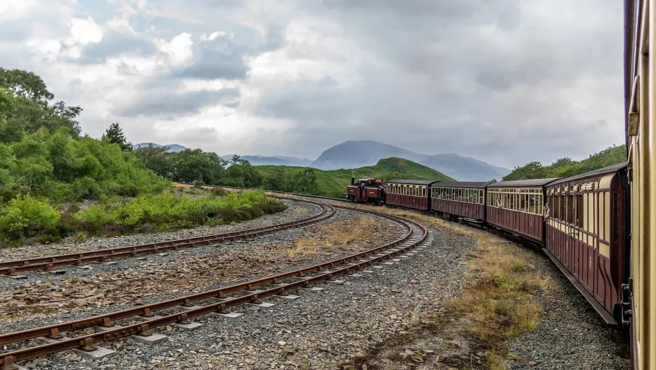 Wales landschap waarbij een rode trein door de heuvel van Wales rijdt.