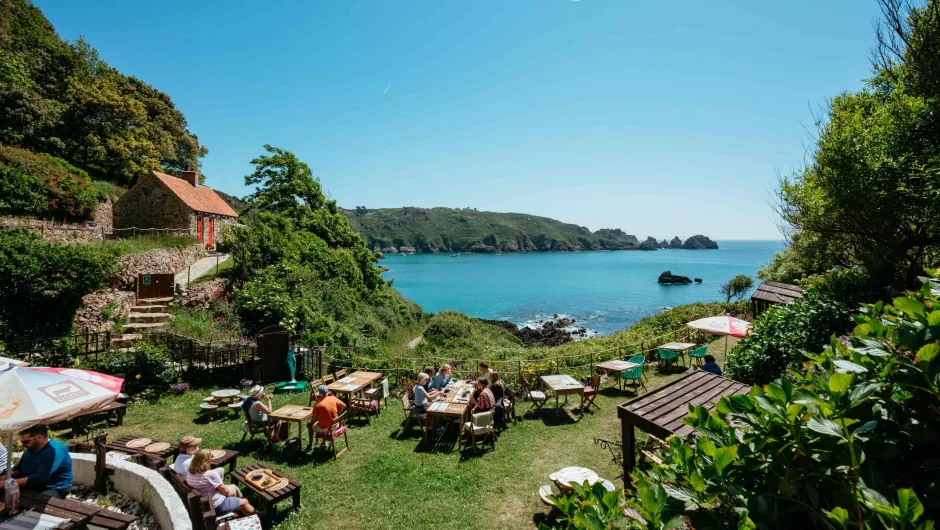 Bestemmingsinfo Kanaaleilanden - toeristen aan tafeltjes in de Moulin Huet baai op Guernsey.