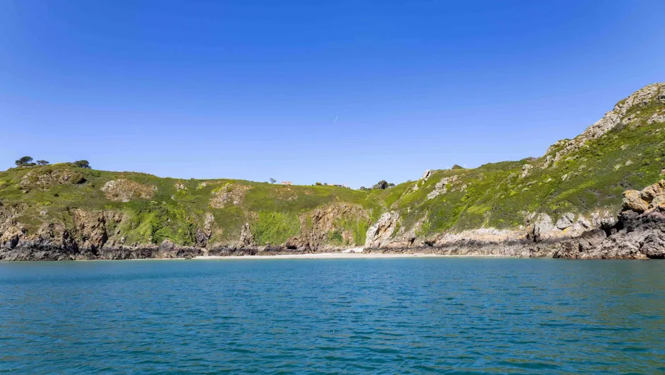 Rondreis Kanaaleilanden groene kliffen en een klein strand aan helderblauwe zee.