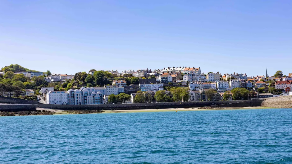 Het uitzicht op Saint Peter Port, de hoofdstad van Guernsey, met zijn charmante gebouwen langs de kustlijn en de heldere blauwe zee.
