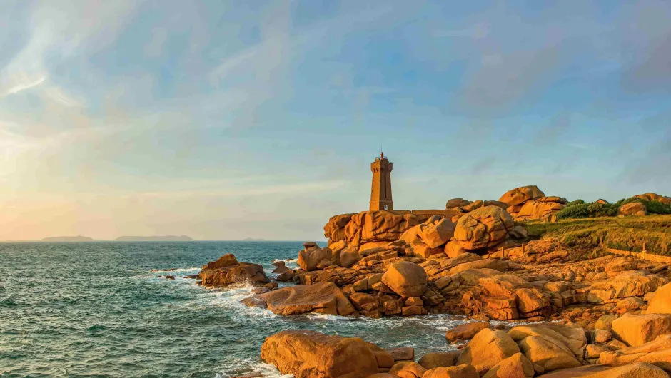 Een roze gloed van de zonsondergang schijnt op de Roze Granietkust van Bretagne, met op de klif een stenen vuurtoren.