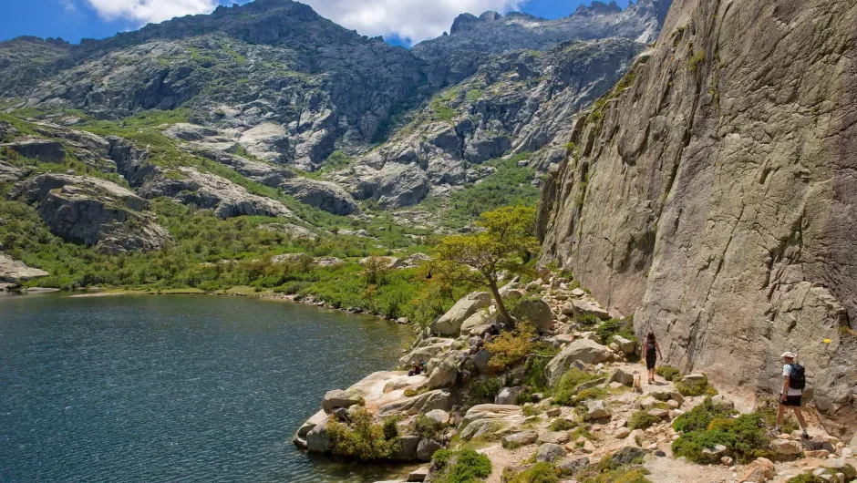 Een wandelpad langs een bergmeer slingert tussen hoge rotswanden, terwijl wandelaars genieten van het indrukwekkende berglandschap.