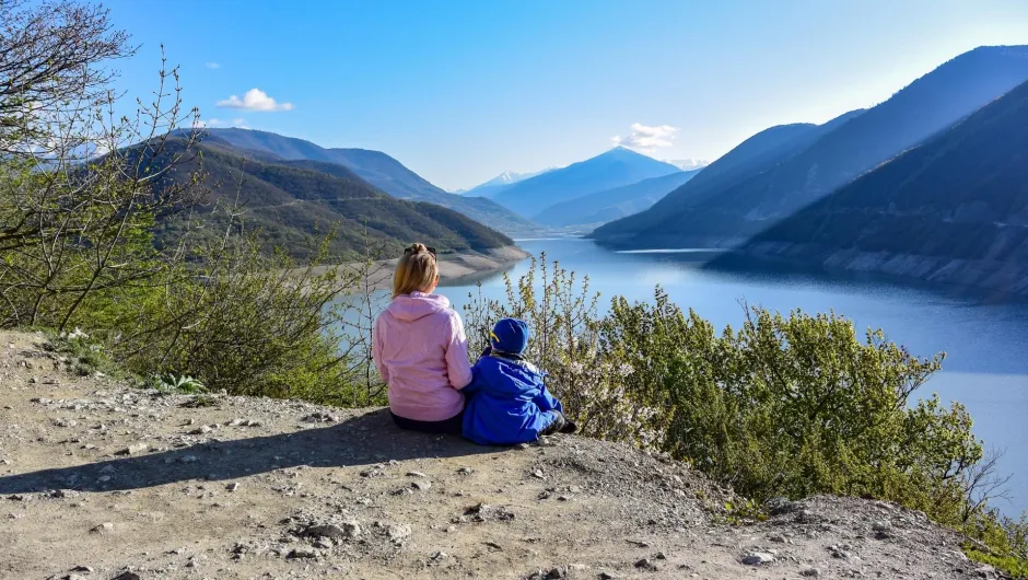 Twee kinderen die zitten op een rots uitkijkend op een uitzicht met bergen en een meer.