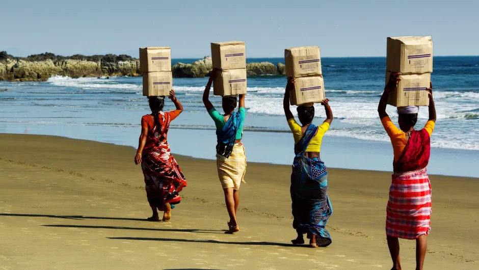 Reistips India - vier lokale vrouwen met dozen op hun hoofd op het strand in Goa.
