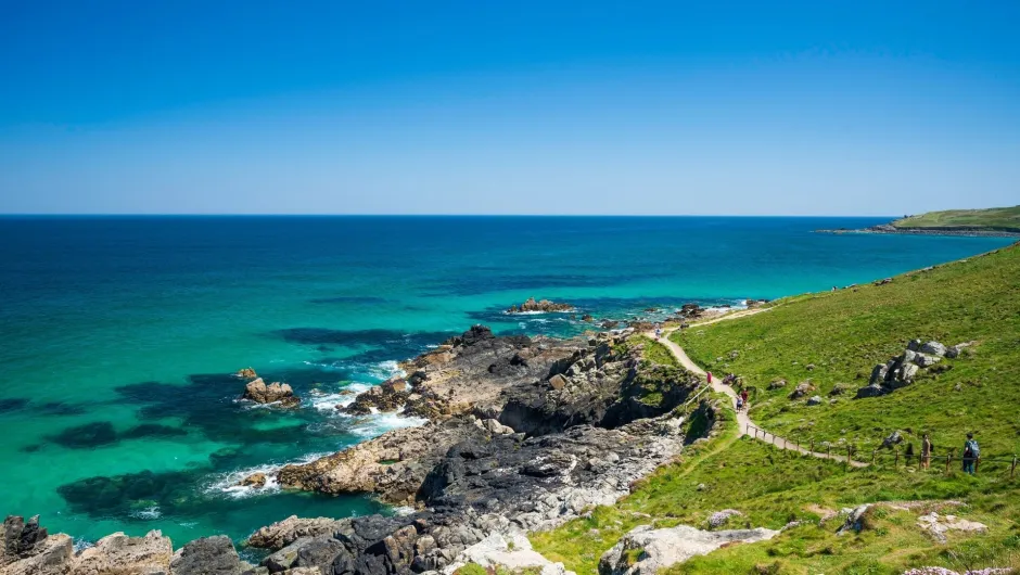 Kust met rotsen en groene weide aan een blauw groene zee.