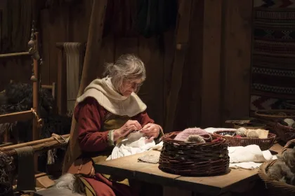 Vrouw in viking dorp die aan het breien is.