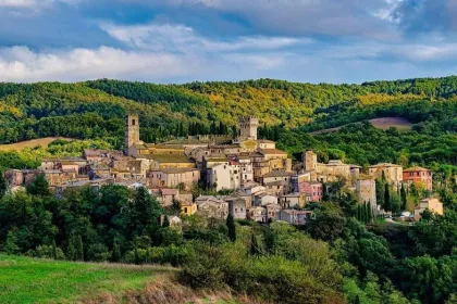 Middeleeuws dorp op een heuvel in Toscane, met stenen huizen en torens, omringd door groene heuvels en bossen onder een deels bewolkte lucht.
