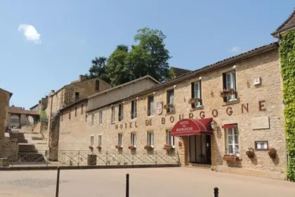Kleinschalig stenen hotel in Cluny met rode letters van de naam en een groene muur van de klimop plant.