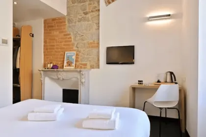 Een eenvoudige en moderne hotelkamer met een bed, een kleine werkplek en een decoratieve schouw straalt rust en comfort uit.