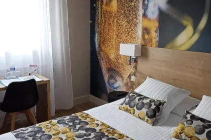 Een comfortabele hotelkamer met een tweepersoonsbed en een opvallende wanddecoratie van een bruisend glas champagne, gecombineerd met warme kleuren en veel natuurlijk licht.