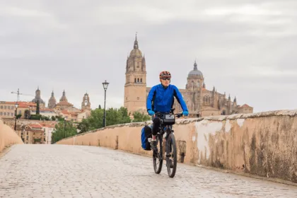 Mannelijke fietser op een brug met daarachter de stad Salamanca.