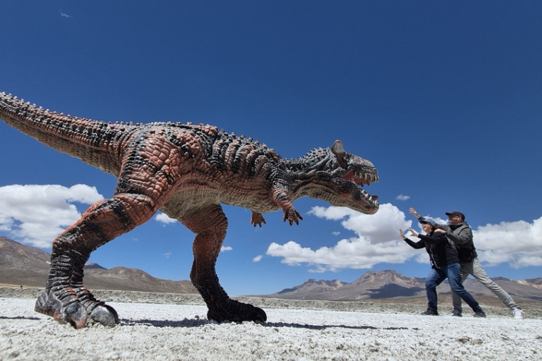 Twee mensen staan met een dinosaurus geposeerd. 