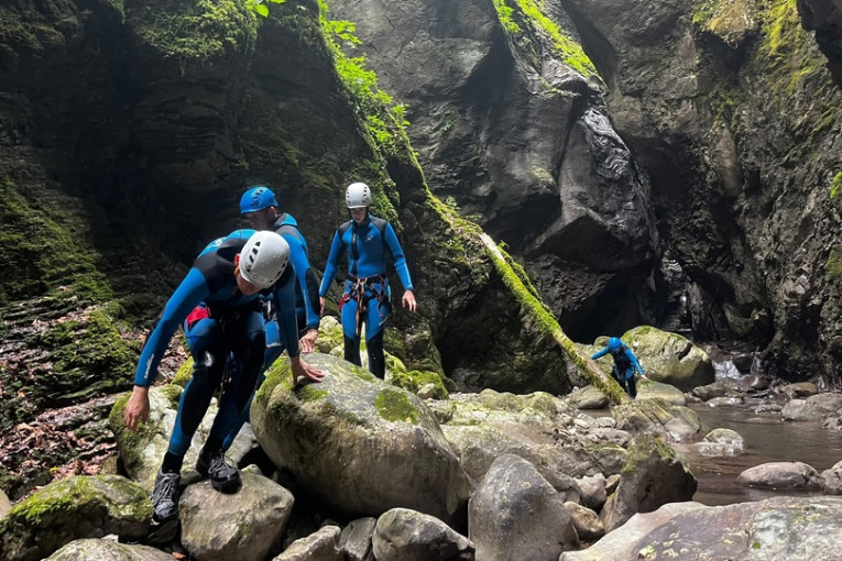 Reizigers in wetsuits en helmen klauteren tijdens het canyoning over rotsblokken in een smalle, groene kloof in Slovenië.