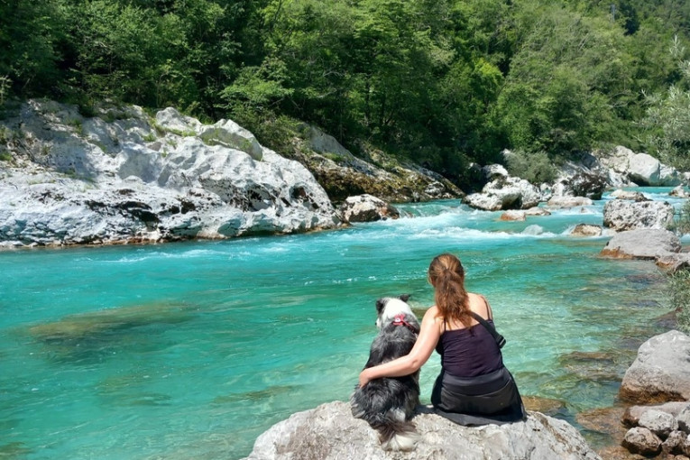 Vrouw zit met een hond op een steen aan het water in Slovenië.