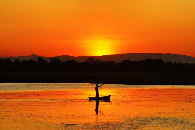 Man is aan het kajakken in Malawi met een mooie zonsondergang.