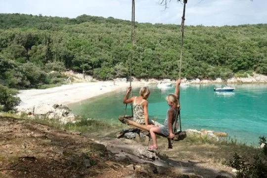 twee kinderen die op een hangstoel buiten zitten, hangende aan een boom bij de zee.