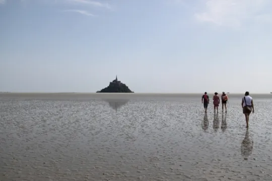 Mensen lopen op het wad richting de Mont Saint-Michel in de verte.