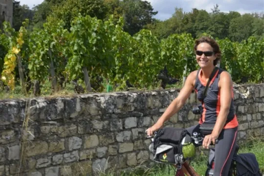 Fietsende vrouw langs wijngaarden die hoger staan op een vlakte wat is aangelegd met stenen.