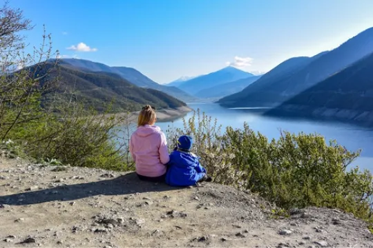 Twee kinderen zittend op een rots kijkend naar een uitzicht met bergen en een meer.