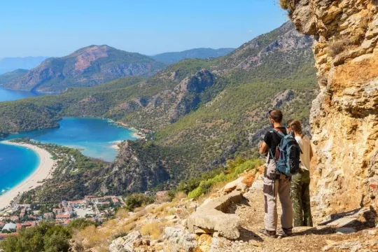 Twee reizigers wandelen de Lycian Way in Turkije en staan stil bij de kust om naar het uitzicht te kijken.
